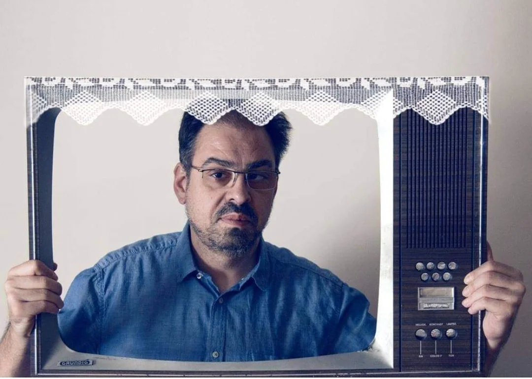 Michael Economou, founder of oncut, looking out through the frame of an old television set.